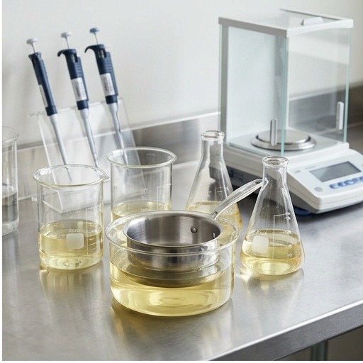 Laboratory leach-test setup with glass beakers, pipettes, and a stainless pan submerged in pale yellow acetic acid solution