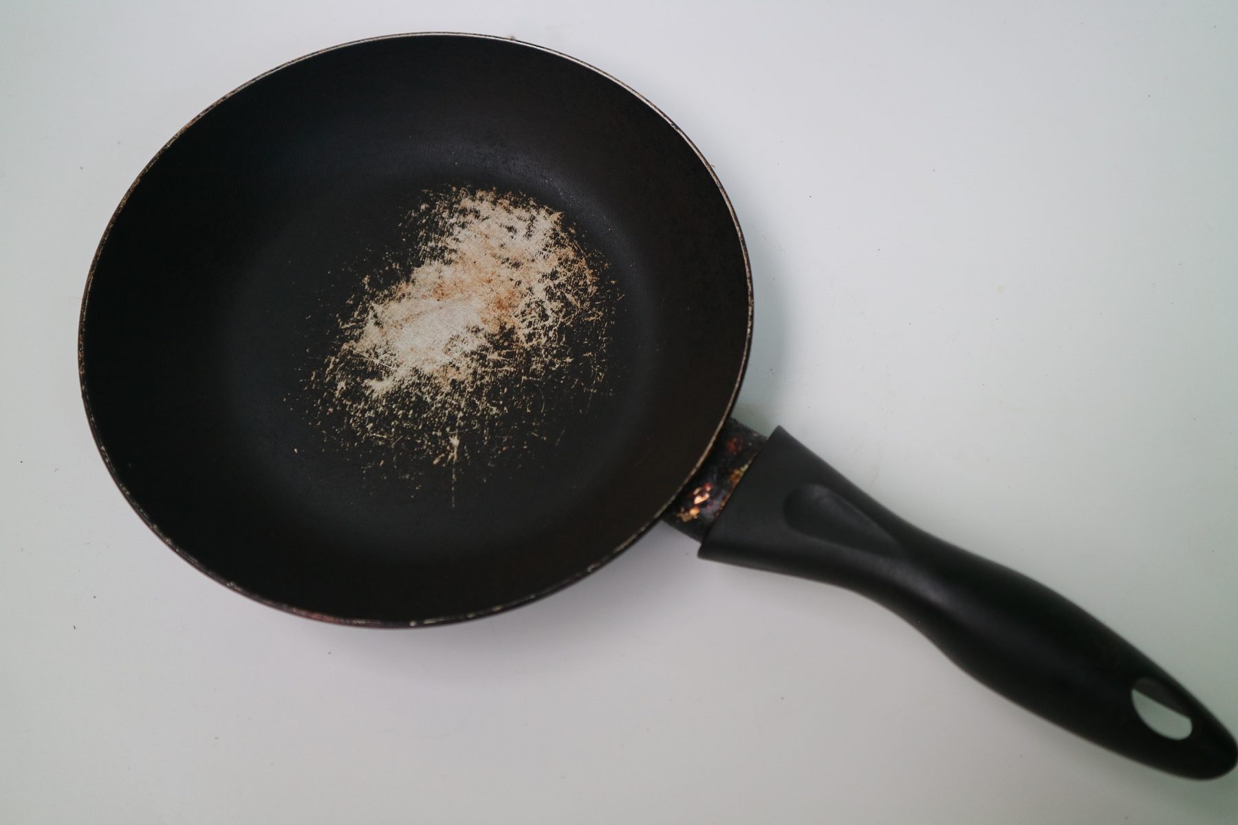 A heavily worn black non-stick pan on white background showing scratched coating
